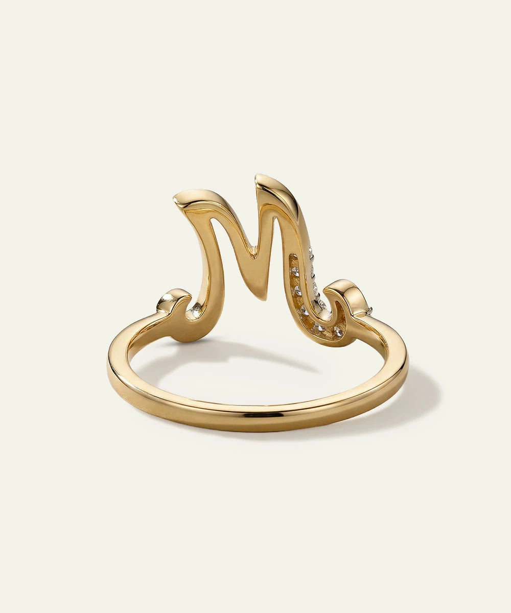 Gold ring with letter 'M' design on a white background