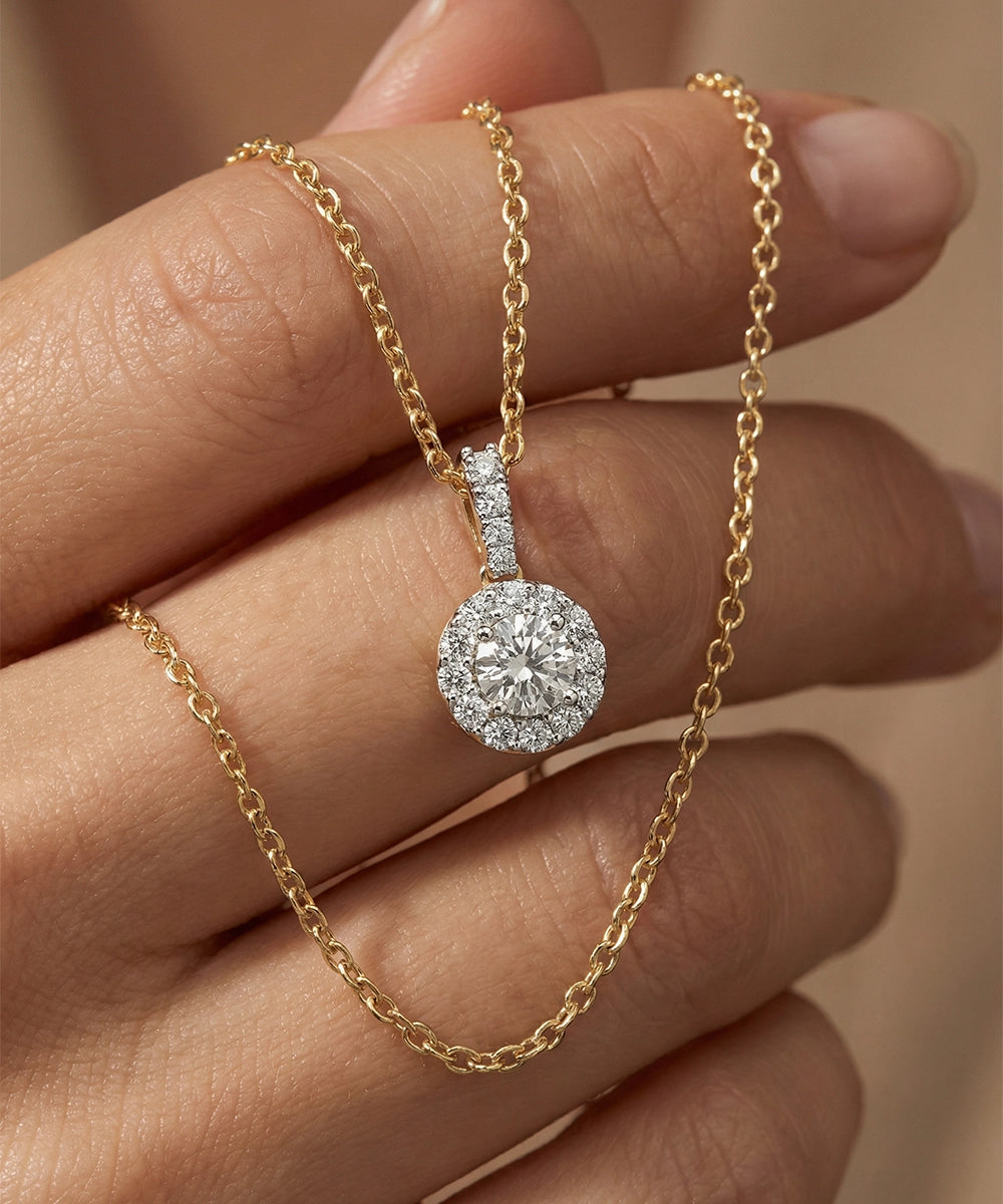 Gold necklace with a diamond pendant held by a hand against a neutral background