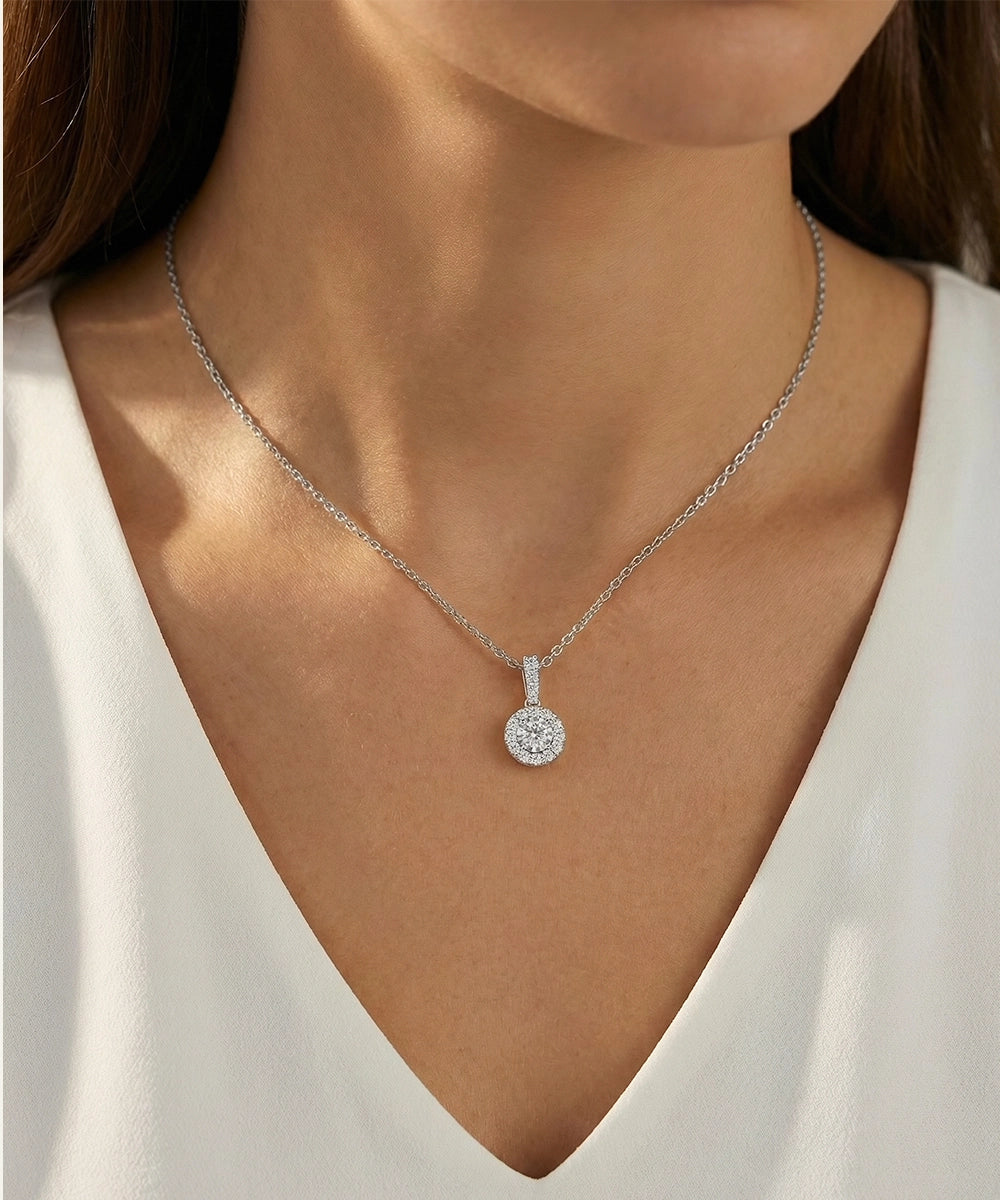 Silver necklace with a diamond pendant worn by a person in a white top.