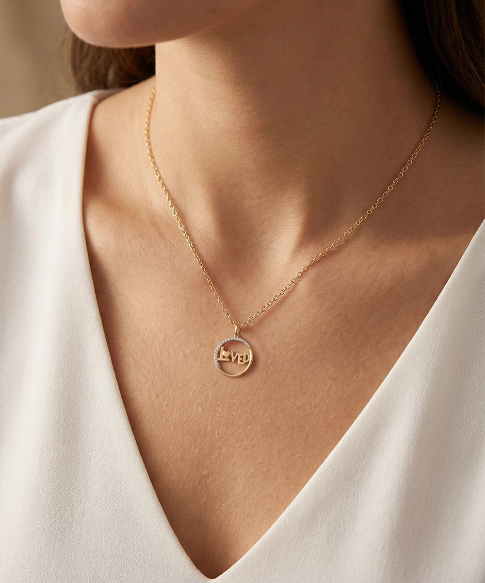 Gold necklace with a round pendant on a person wearing a white top.