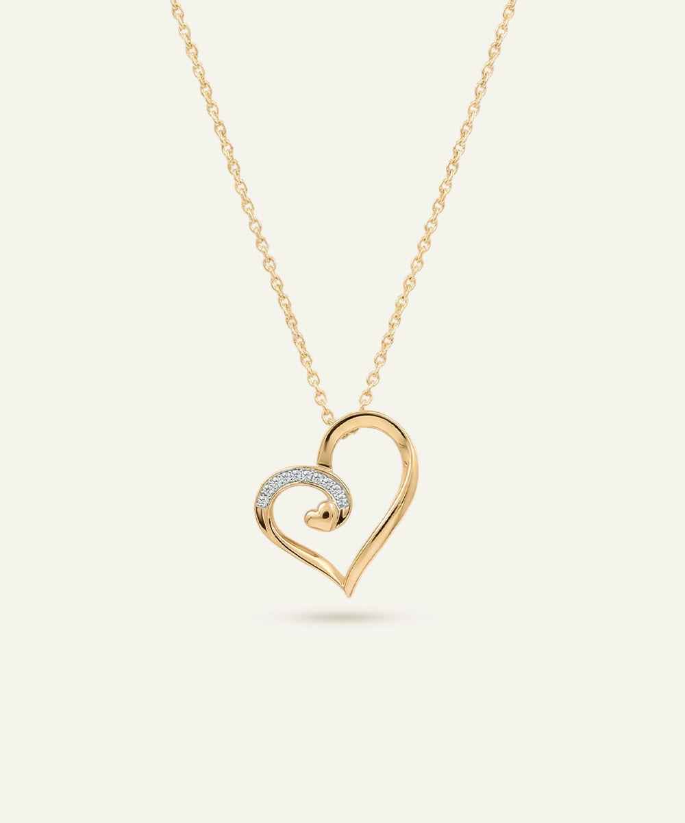 Gold heart-shaped necklace with a smaller heart pendant on a light beige background