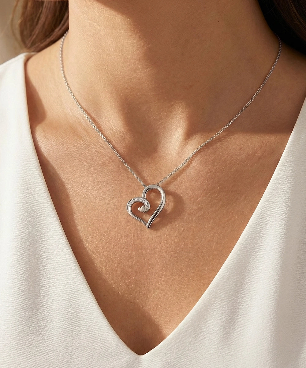 Silver heart-shaped necklace with a diamond on a person wearing a white top.