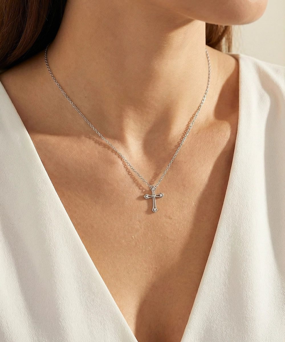 Silver cross necklace on a person wearing a white top