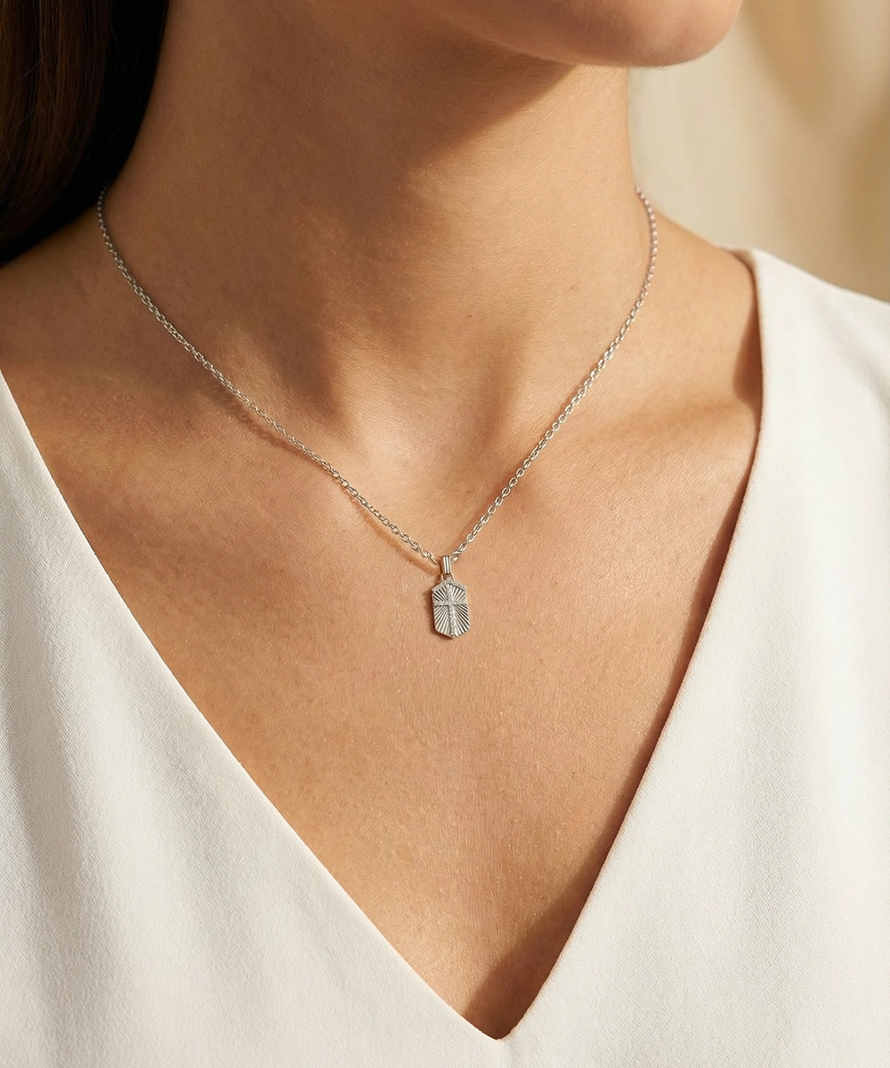 Silver necklace with a pendant worn by a person in a white top.