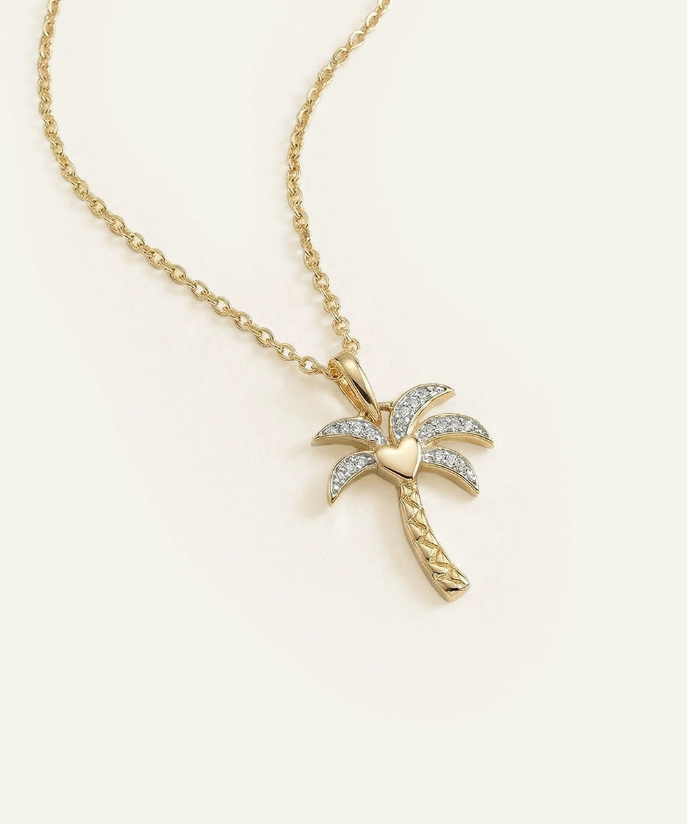 Gold palm tree necklace with diamond accents on a beige background