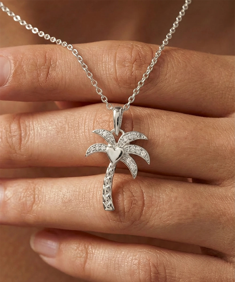 Silver palm tree necklace held between fingers