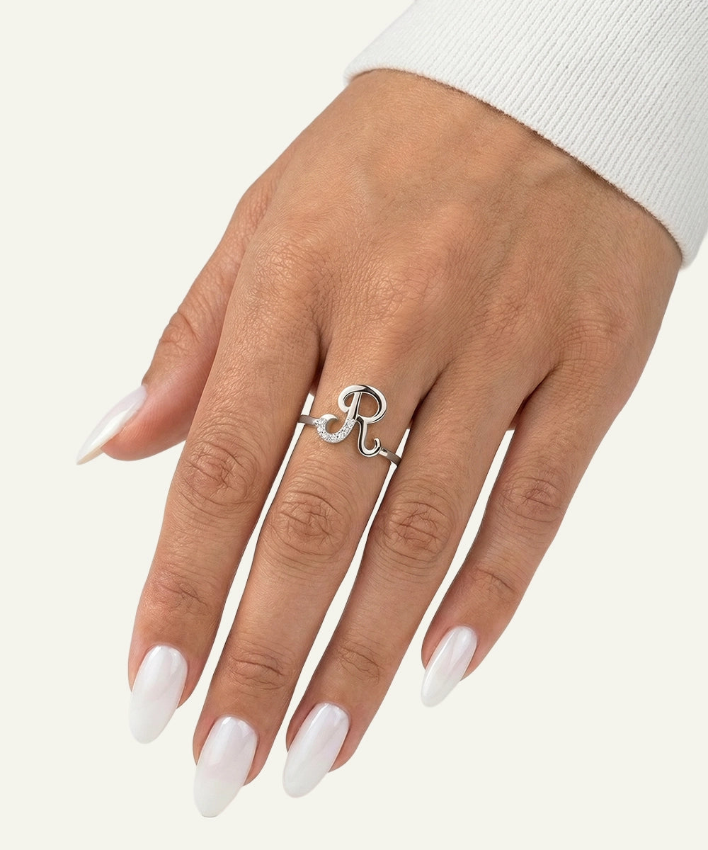 Hand wearing a silver ring with a heart and 'R' design on a white background