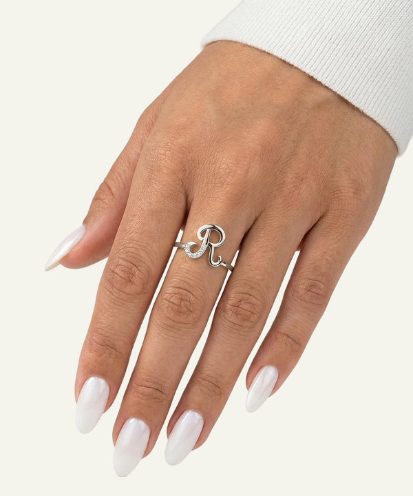Hand wearing a silver ring with a heart and 'R' design on a white background