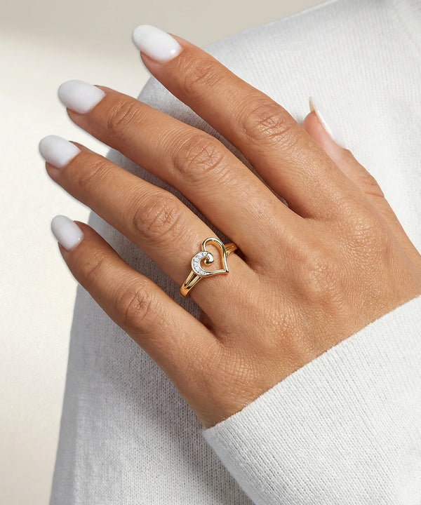 Hand wearing a gold ring with a heart design on a light background