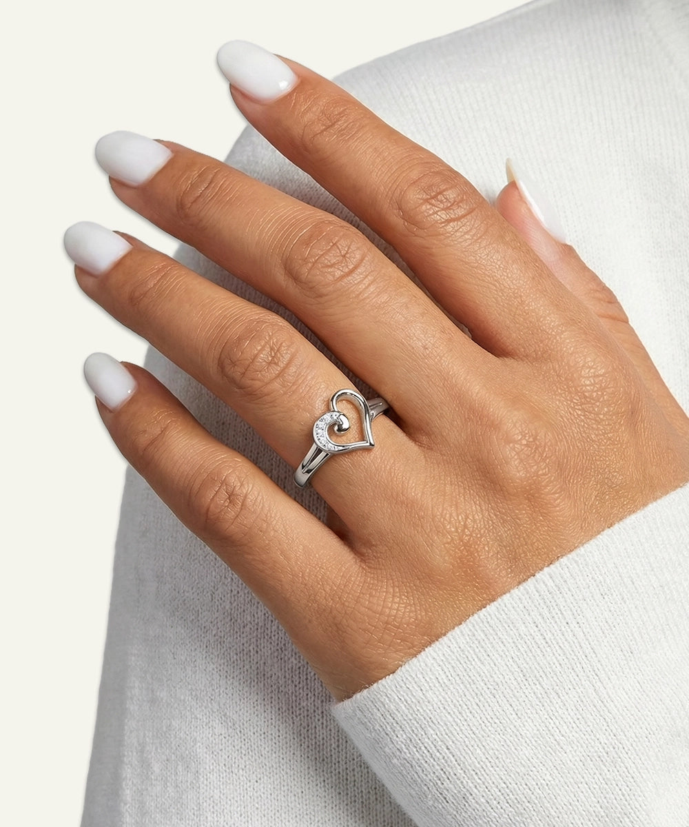 Hand wearing a silver heart-shaped ring on a white background