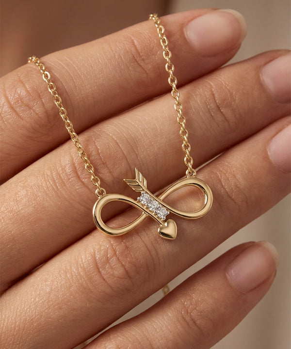 Gold necklace with an infinity symbol and heart pendant on a hand against a neutral background