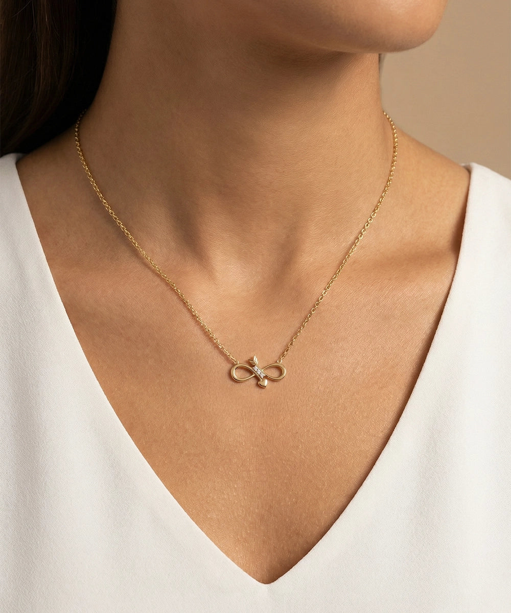 Gold necklace with a pendant on a person wearing a white top against a neutral background