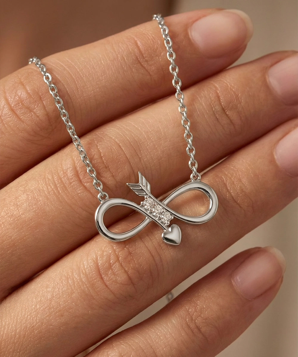Silver necklace with an infinity symbol and heart pendant on a hand against a neutral background