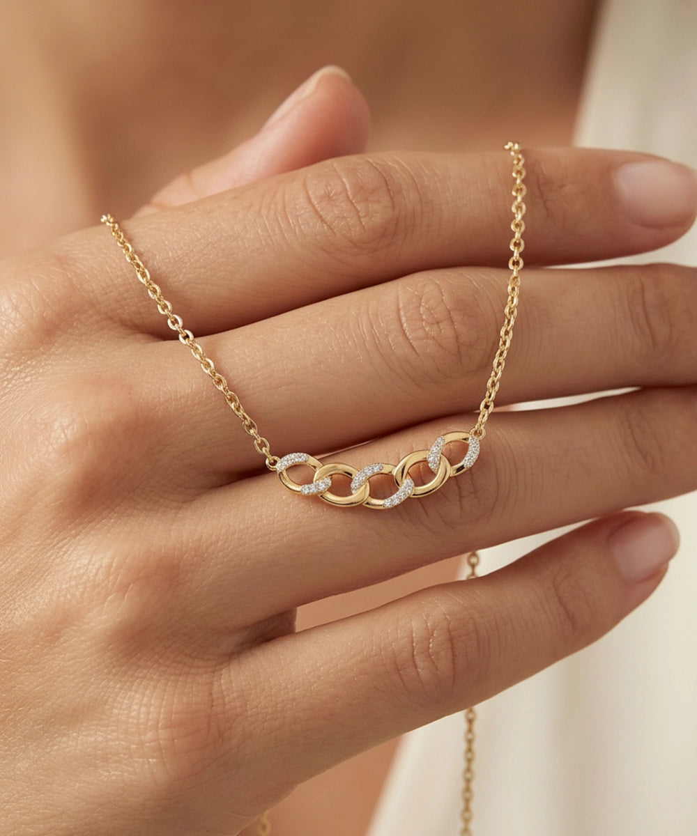 Gold necklace with interlocking rings on a hand against a neutral background