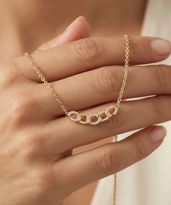 Gold necklace with interlocking rings on a hand against a neutral background