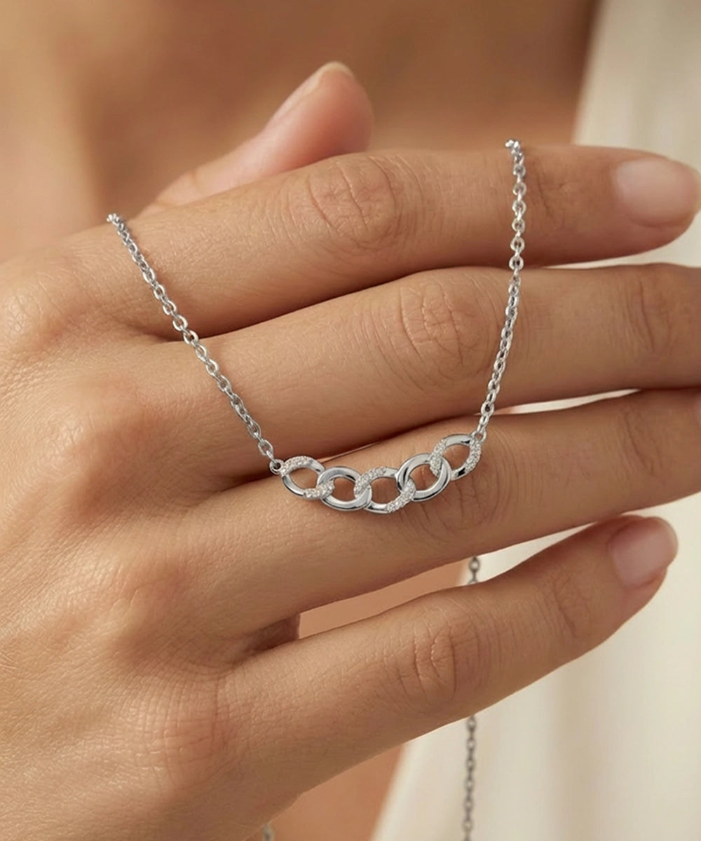 Silver necklace with interlocking rings on a hand against a neutral background