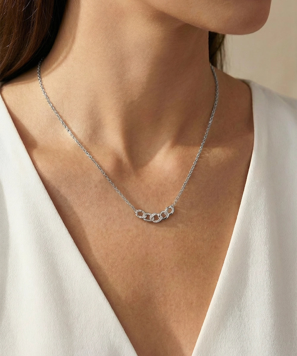Silver necklace on a person wearing a white top against a neutral background