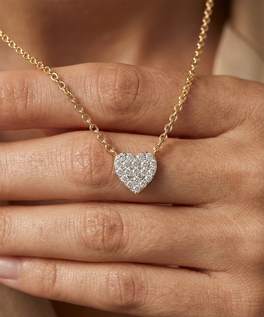 Heart-shaped diamond pendant on a gold chain held by a hand