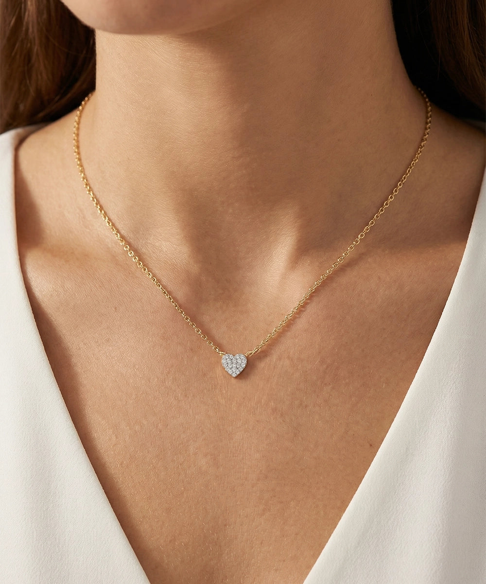 Gold necklace with a heart-shaped pendant on a person wearing a white top.