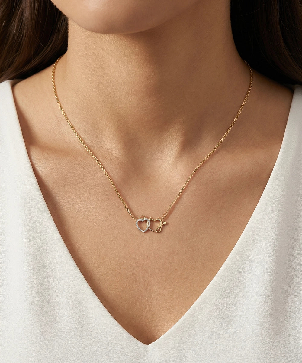 Gold necklace with interlocking heart pendants on a person wearing a white top.