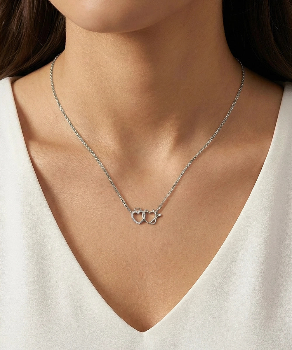 Silver necklace with a heart pendant worn by a person in a white top.
