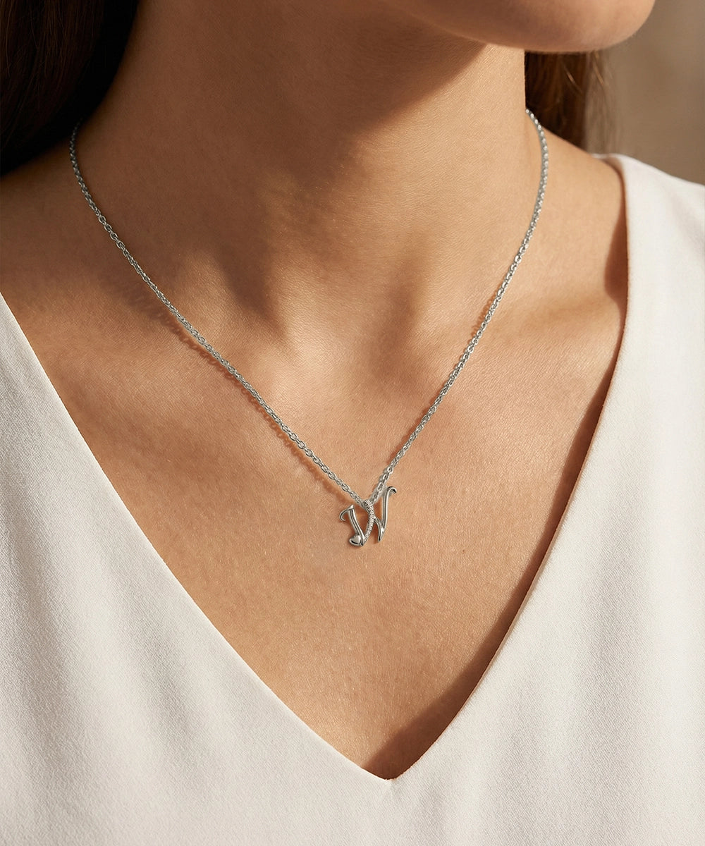 Silver necklace with a heart pendant worn by a person in a white top.