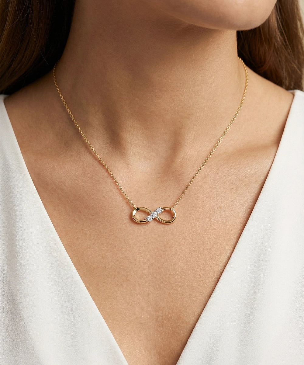 Gold necklace with a heart and diamond pendant worn by a person in a white top.