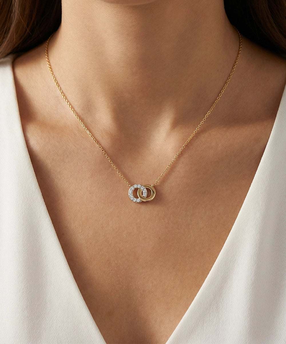 Gold necklace with a circular pendant on a person wearing a white top.