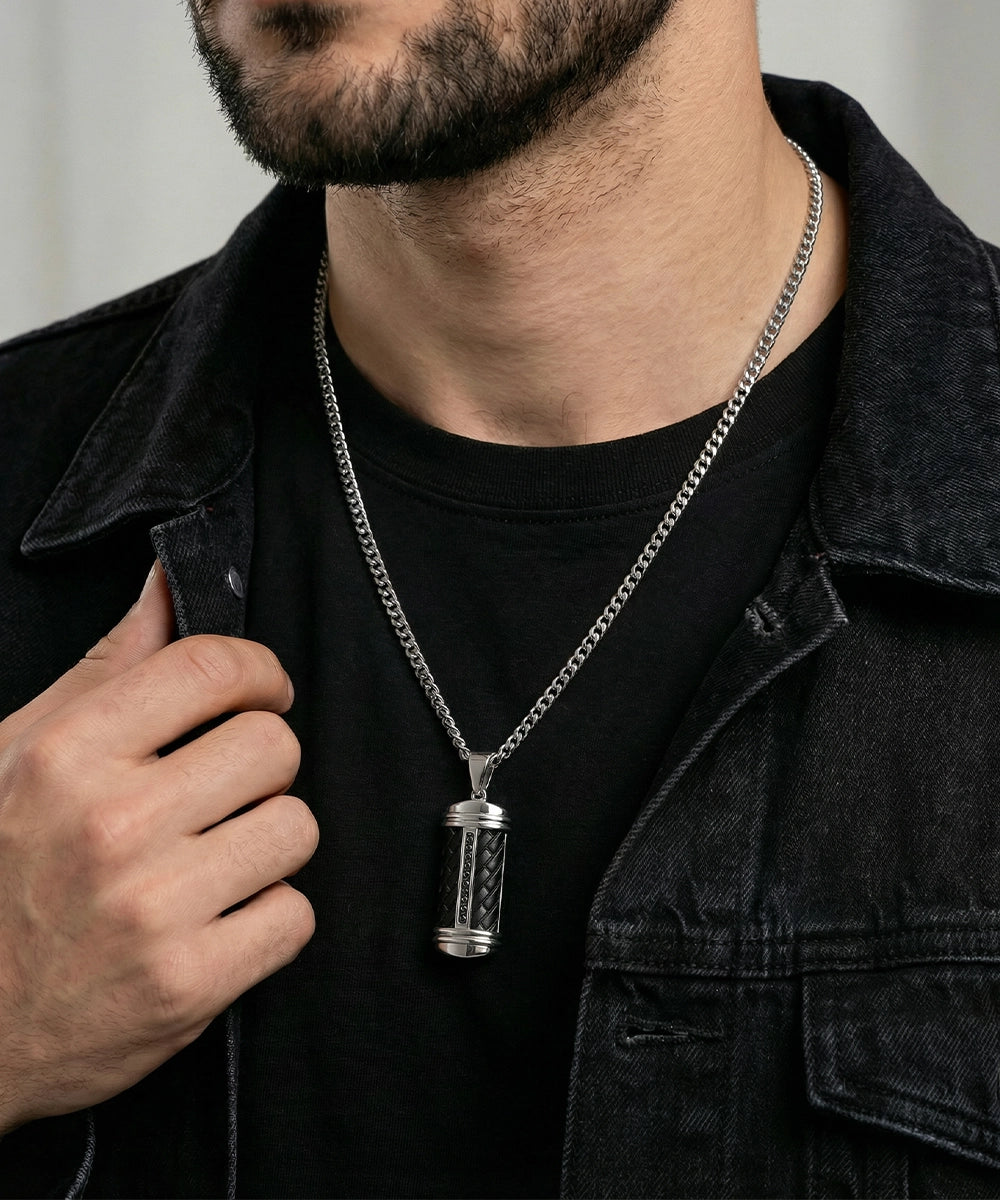 Man wearing a black jacket with a silver necklace featuring a pendant.