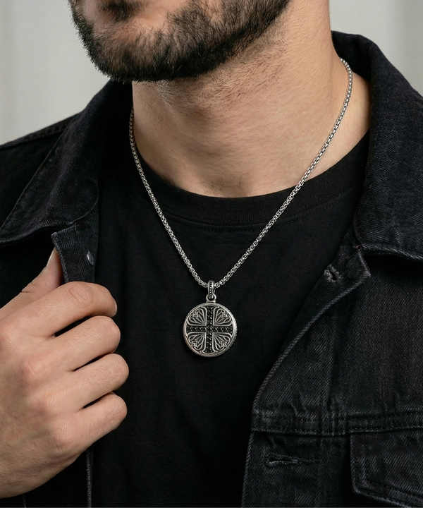 Man wearing a black shirt and dark jacket with a silver necklace featuring a circular pendant.