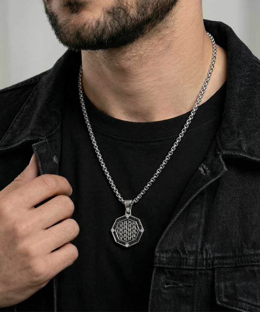 Man wearing a black shirt and dark jacket with a silver necklace featuring a detailed pendant.