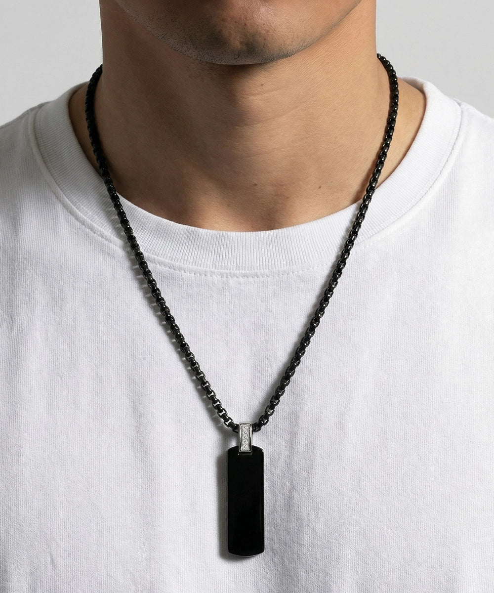 Person wearing a black necklace with a pendant on a plain background