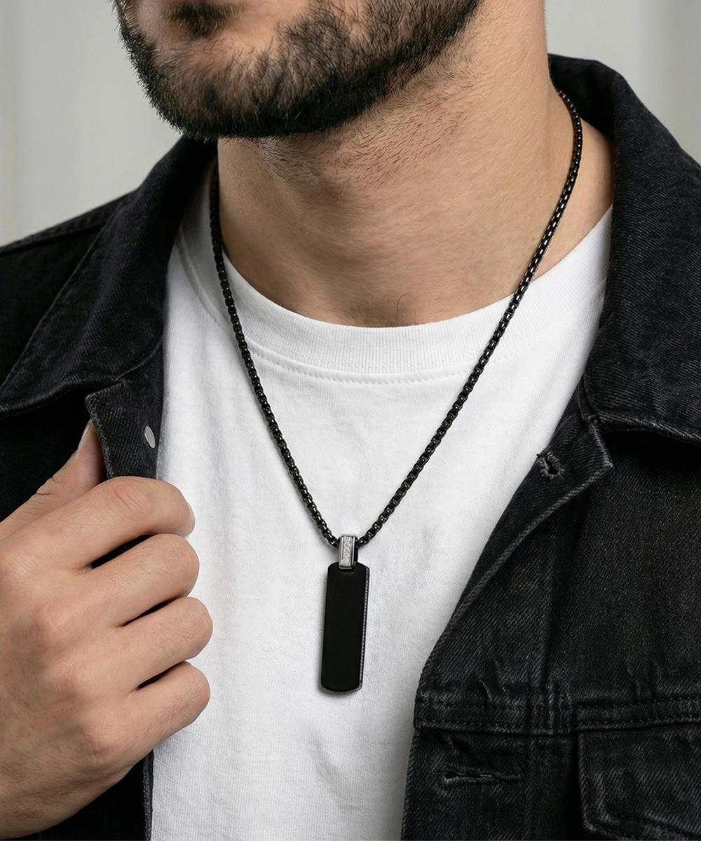 Man wearing a black dog tag necklace with a white shirt and dark jacket.