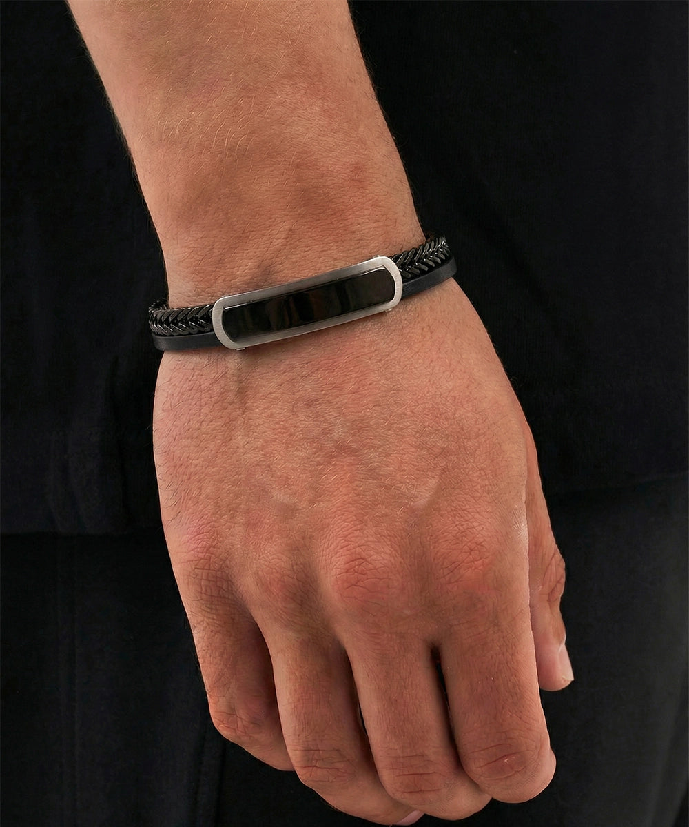 Black leather bracelet with a silver clasp on a wrist against a black background
