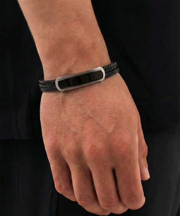 Black leather bracelet with a silver clasp on a wrist against a black background