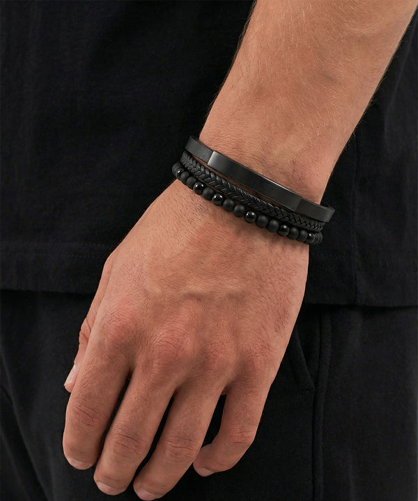 Close-up of a wrist wearing multiple black bracelets on a plain background