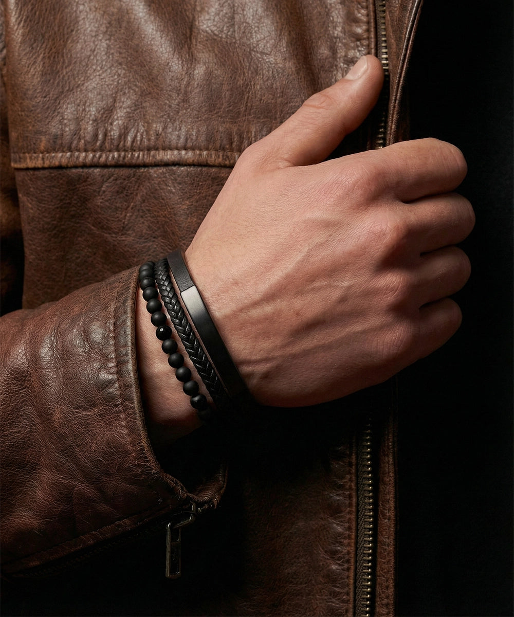 Close-up of a hand wearing bracelets on a brown leather jacket.