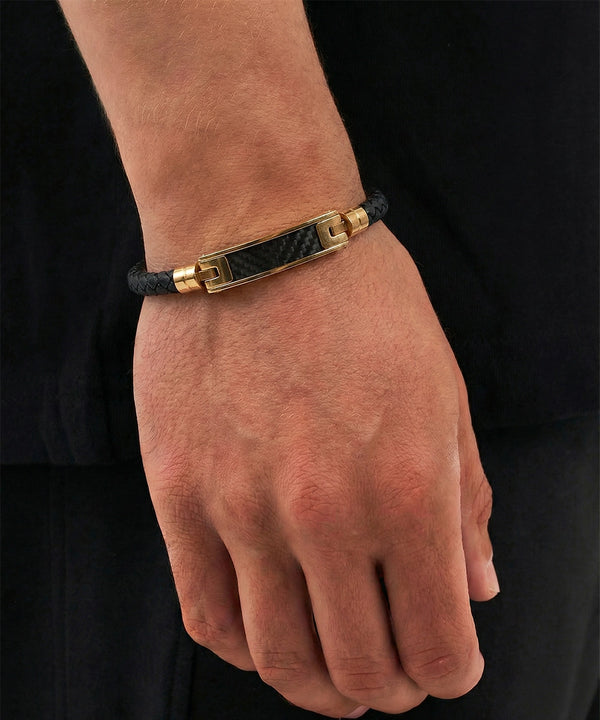 Hand wearing a black leather bracelet with a gold clasp on a black background
