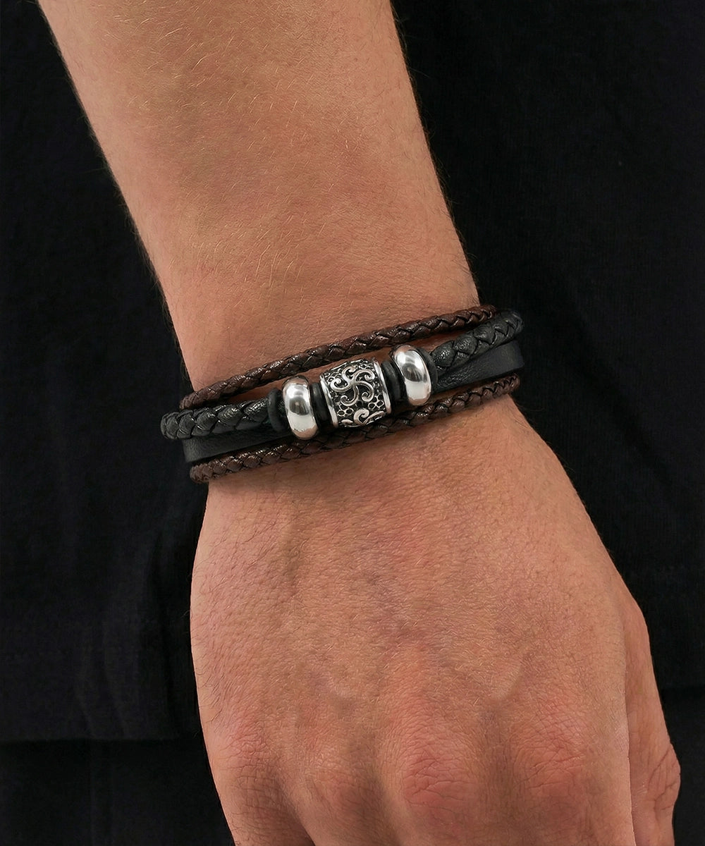 Close-up of a wrist wearing a black leather bracelet with silver beads against a dark background