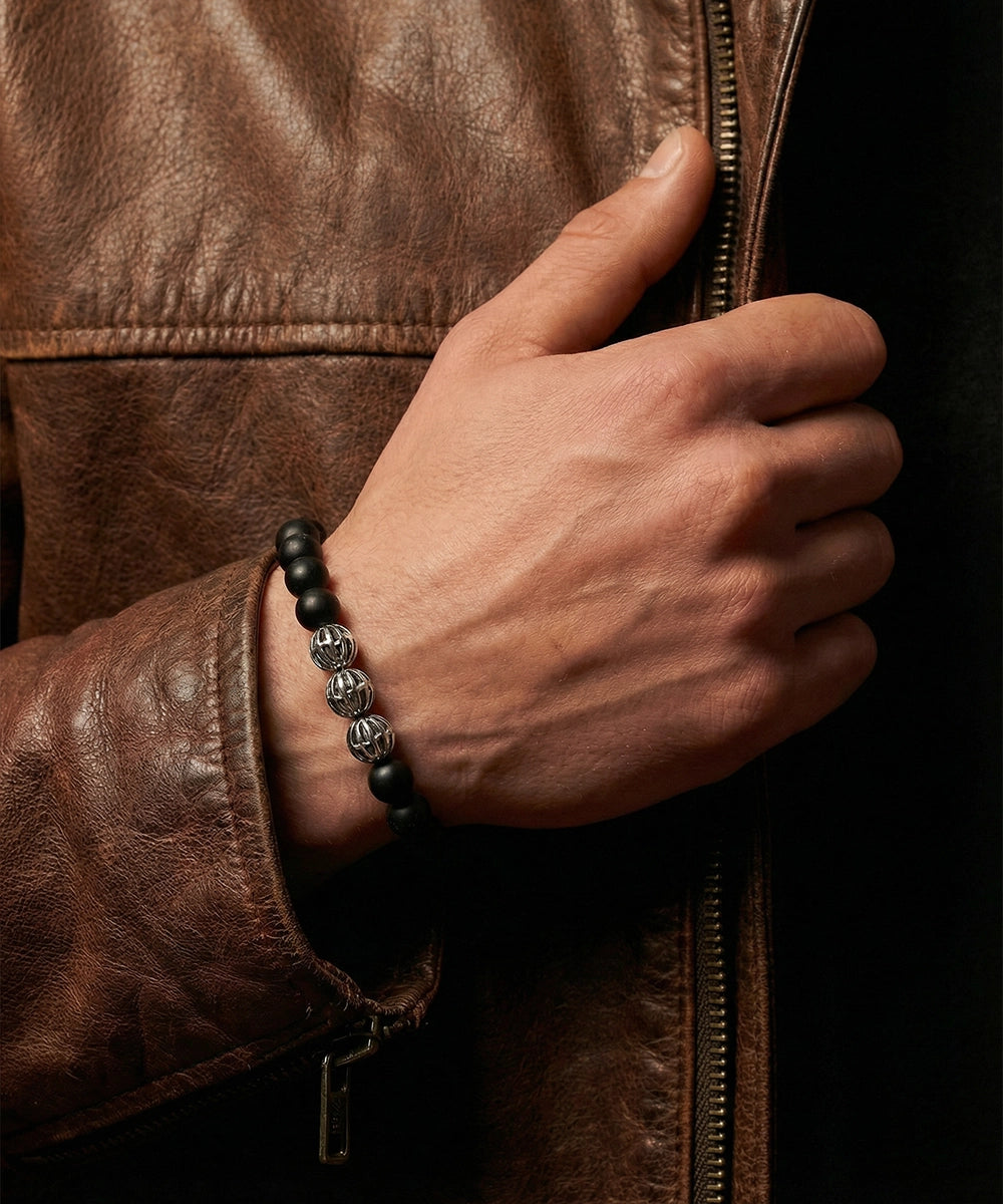 Hand wearing a black beaded bracelet on a brown leather jacket background