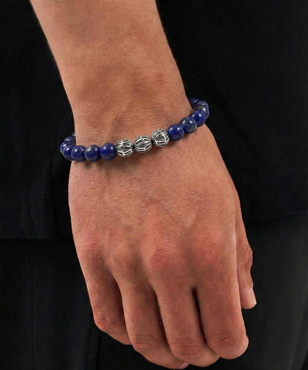 Hand wearing a blue beaded bracelet with silver accents on a black background