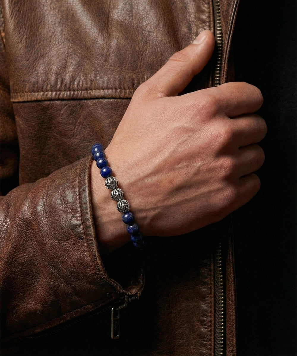 Hand wearing a blue beaded bracelet on a brown leather jacket.