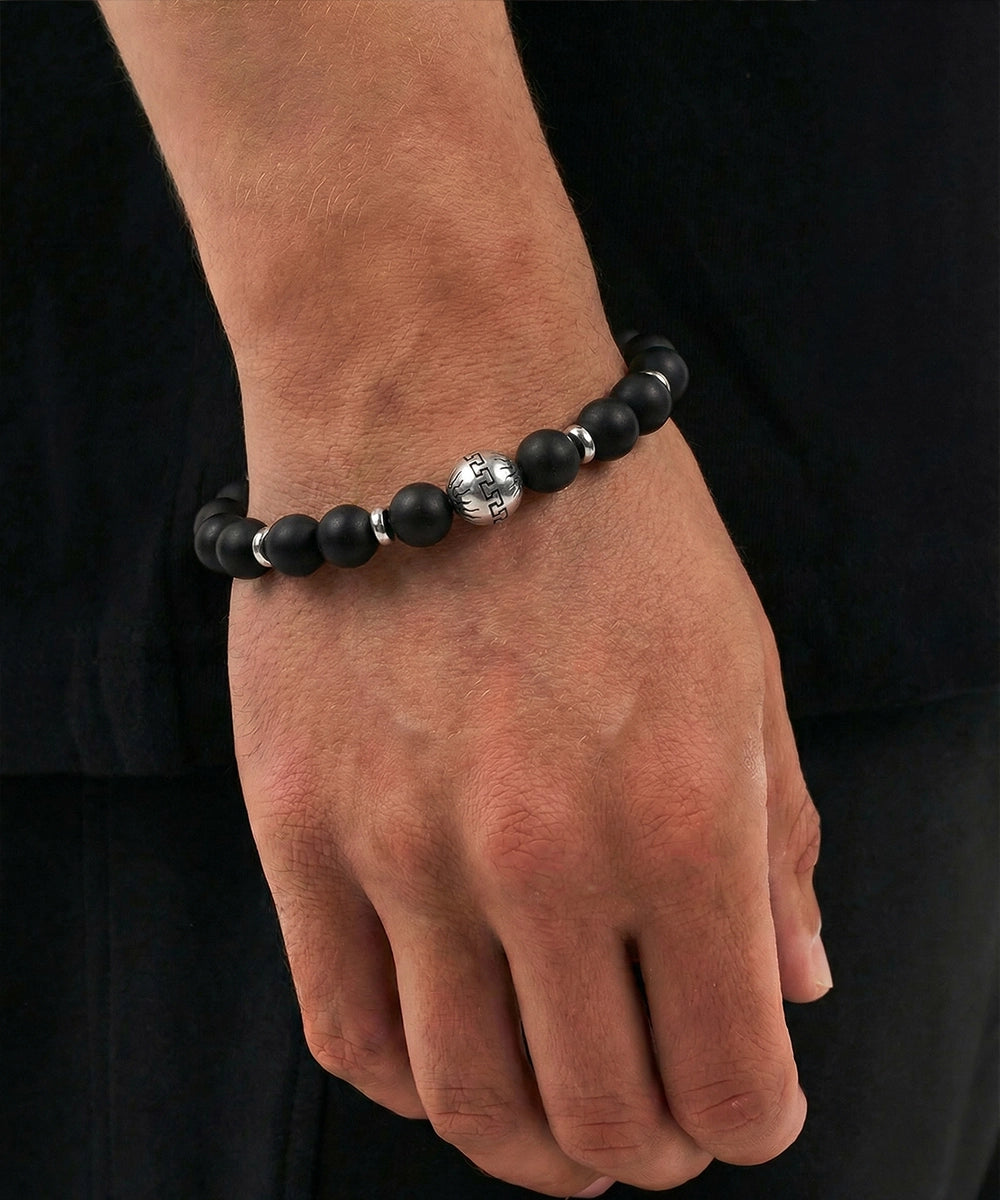 Hand wearing a black beaded bracelet with a silver clasp on a black background