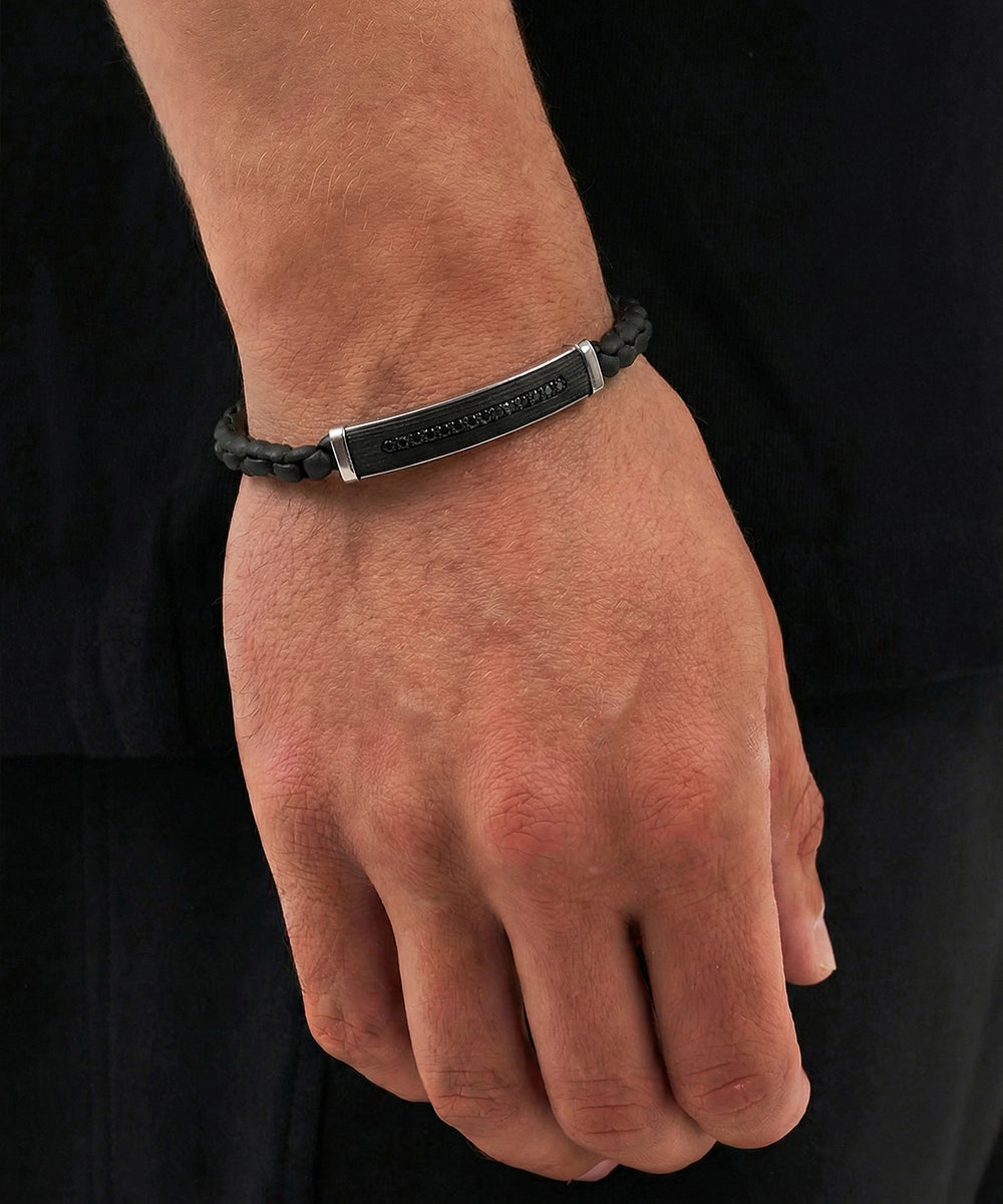 Black leather bracelet with a metal tag on a wrist against a black background