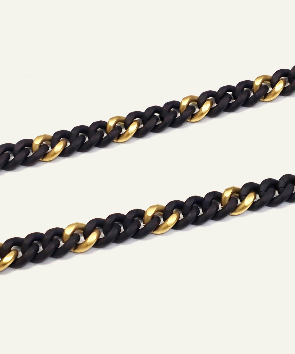Two chain necklaces, one black and one gold, on a light gray background.