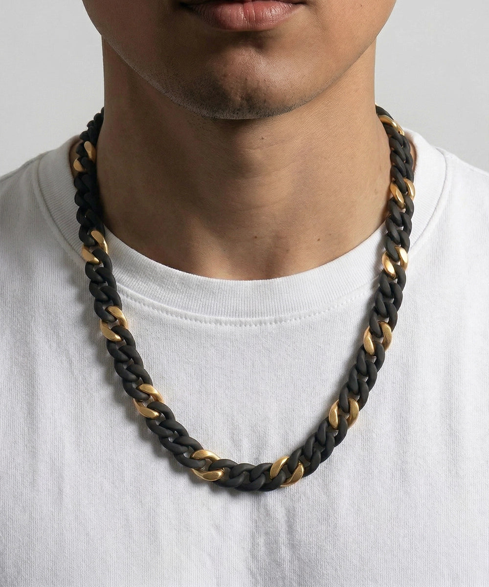 Person wearing a black and gold braided necklace on a plain background