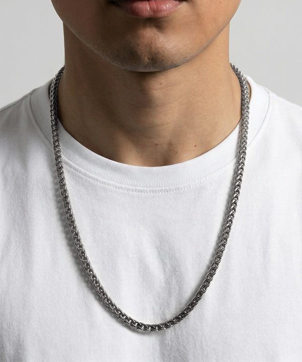 Person wearing a silver chain necklace on a plain background