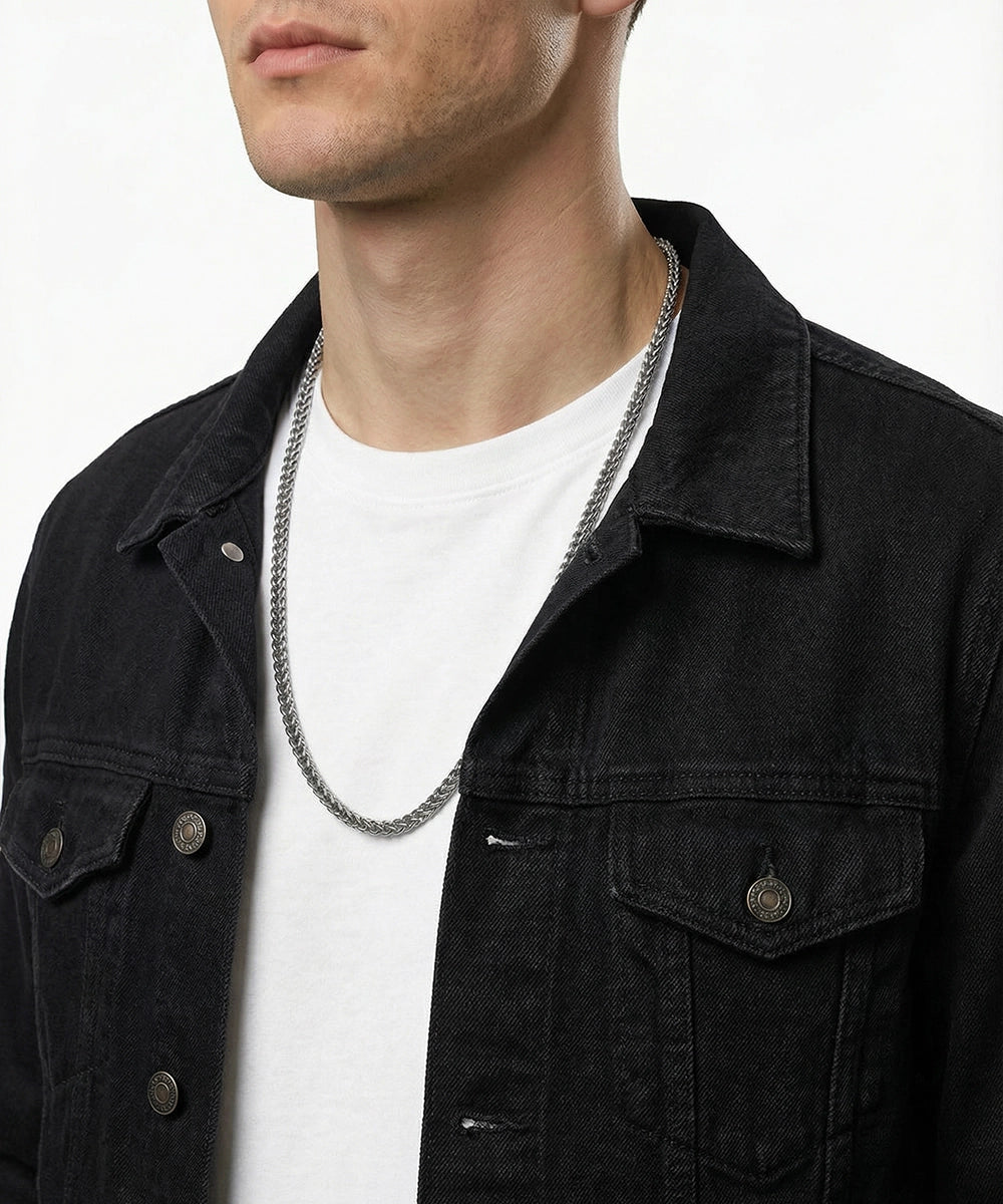 Person wearing a black denim jacket and white shirt with a silver chain necklace.