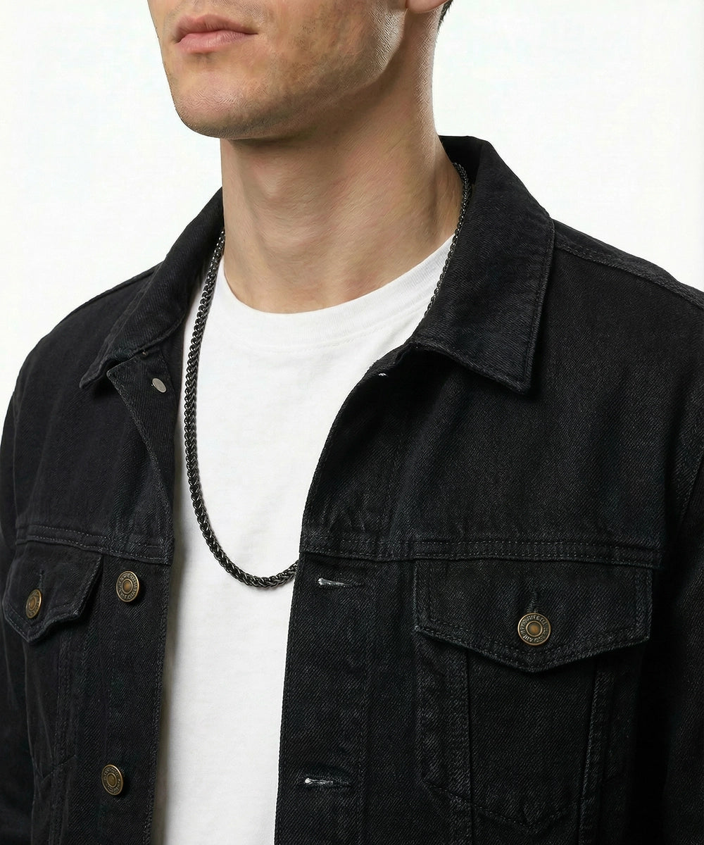 Person wearing a black jacket over a white shirt with a necklace.