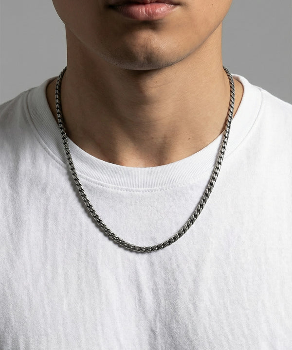 Person wearing a silver chain necklace on a plain background